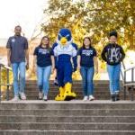 Four students walking down the outdoor steps with Auggie the mascot